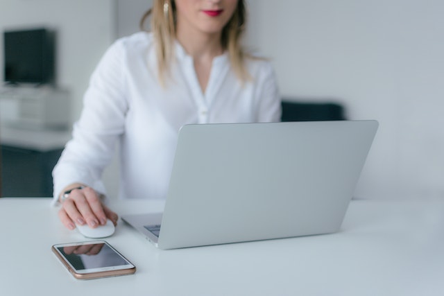 Person in white sitting at a white desk working on a laptop with an external mouse